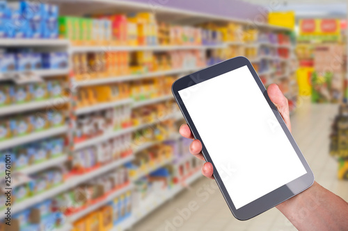 hand holding tablet with blank screen in front of goods shelfs in supermarket