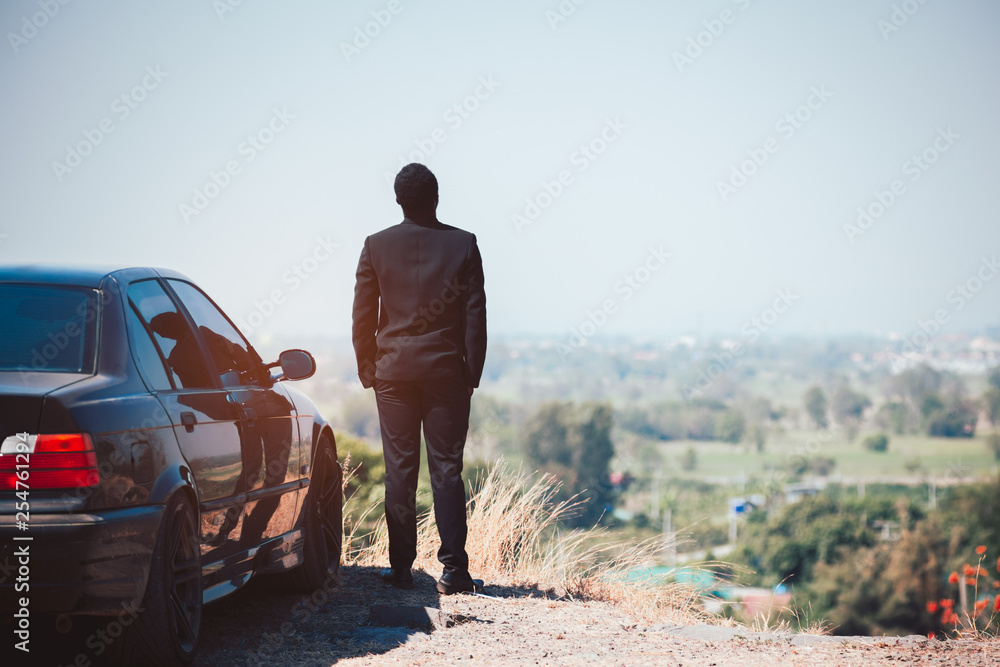 African Businessman standing on top of rock cliff with car African Businessman standing on top of rock cliff with car