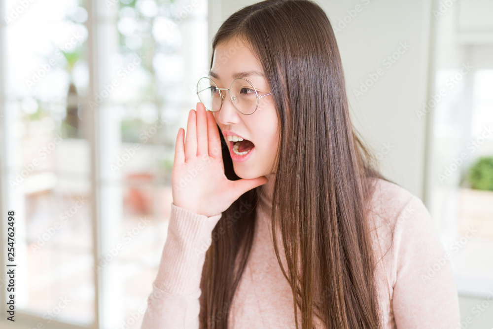 Beautiful Asian woman wearing glasses shouting and screaming loud to side with hand on mouth. Communication concept. Beautiful Asian woman wearing glasses shouting and screaming loud to side with hand on mouth. Communication concept.