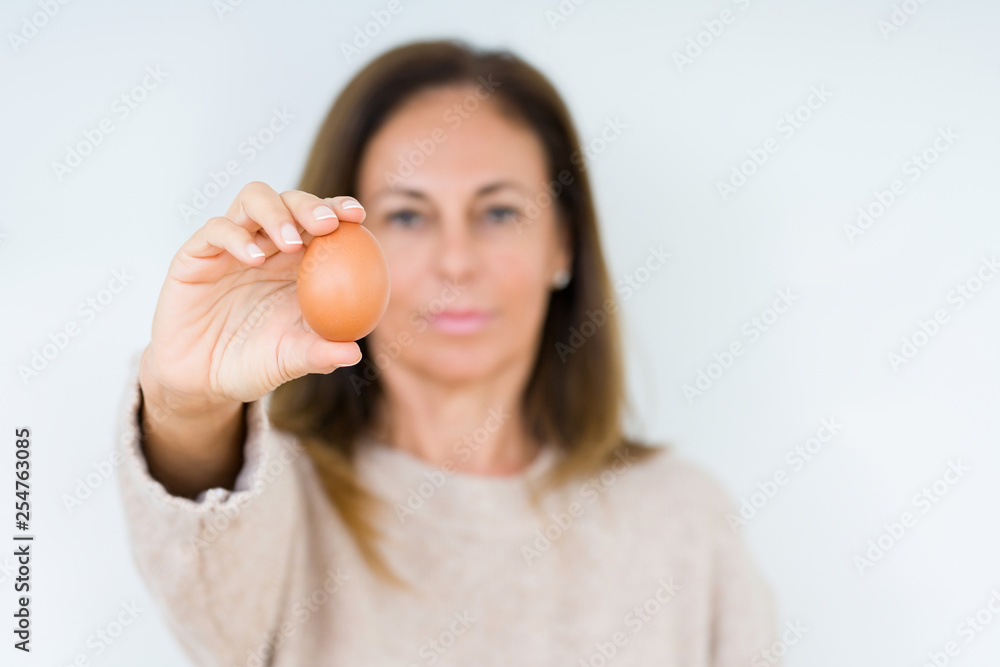 Middle age woman holding fresh egg over isolated background with a confident expression on smart face thinking serious Middle age woman holding fresh egg over isolated background with a confident expression on smart face thinking serious