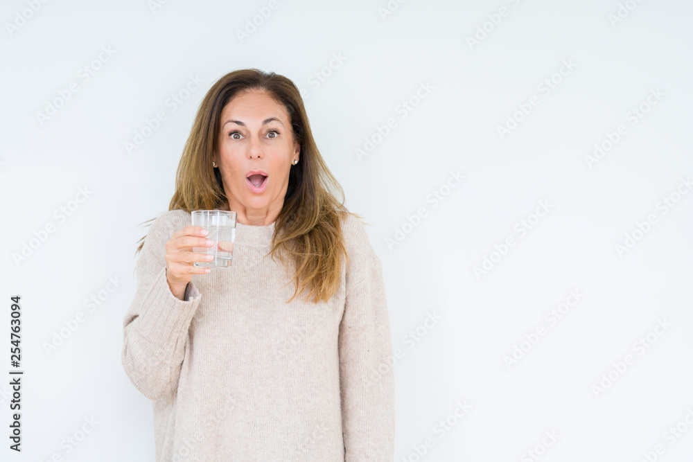 Middle age woman drinking glass of water isolated background scared in shock with a surprise face, afraid and excited with fear expression Middle age woman drinking glass of water isolated background scared in shock with a surprise face, afraid and excited with fear expression