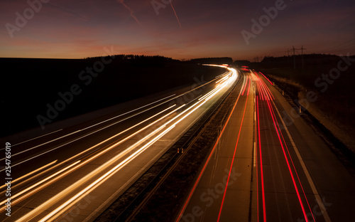 Night urban scene of motion blurred light tracks glowing to the darkness of highway traffic transport to the city just after sunset. Creative long time exposure diagonal composed photography.