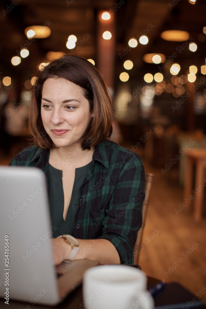 Fototapeta premium Confident businesswoman using laptop computer while sitting against illuminated lights in restaurant