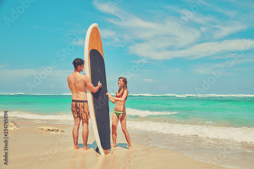 Couple with surfboard enjoying on the tropical beach.