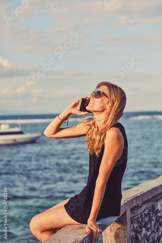 Attractive woman using cellphone while sitting near sea/ocean.