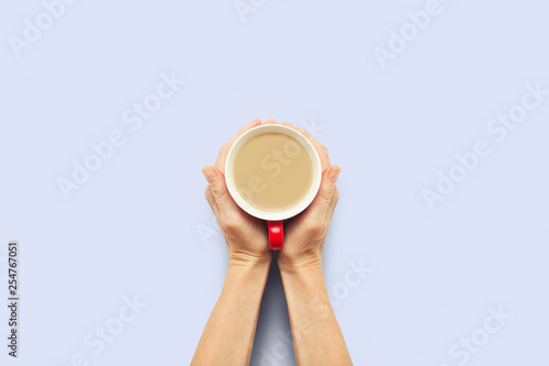 Two hands holding a cup with hot coffee on a blue background. Breakfast concept with coffee or tea. Good morning, night, insomnia. Flat lay, top view photo