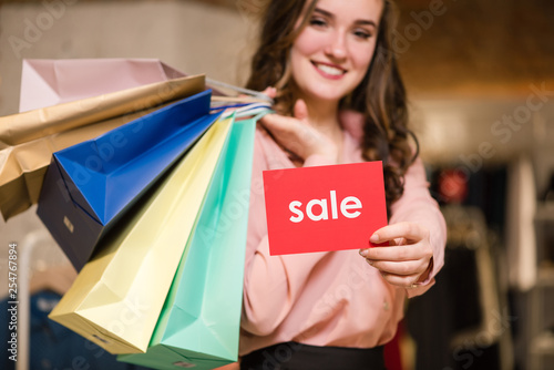 Smiling girl with purchases and sale sign.