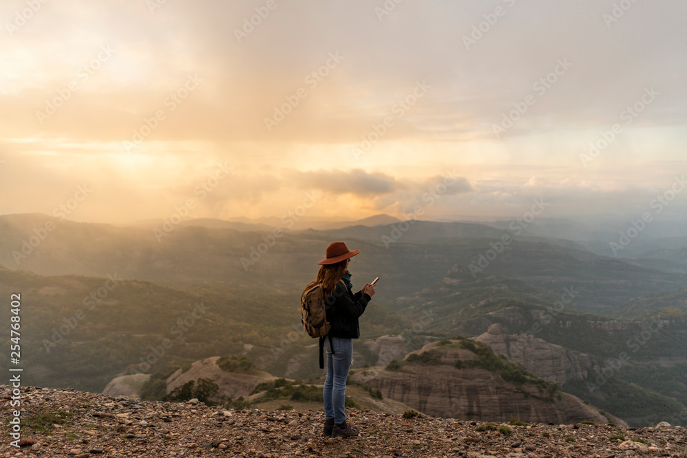 Woman with backpack, standing on mountain, looking at view, using smartphone