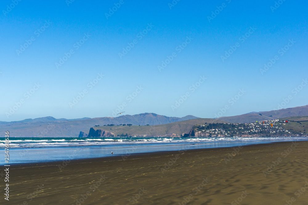 empty vast beach with coastal line and mountains on the horizon line during sunny day