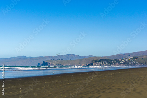 empty vast beach with coastal line and mountains on the horizon line during sunny day