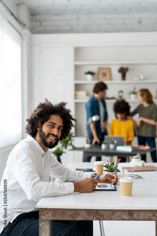Young man working in coworking space, with colleagues discussing in background Young man working in coworking space, with colleagues discussing in background