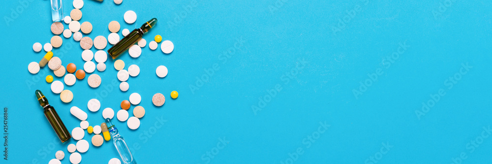 Pills of different colors and ampoules with medicine on a blue background. Concept of the pharmaceutical industry, medicine, treatment and recovery after illness. Banner. Flat lay, top view Pills of different colors and ampoules with medicine on a blue background. Concept of the pharmaceutical industry, medicine, treatment and recovery after illness. Banner. Flat lay, top view