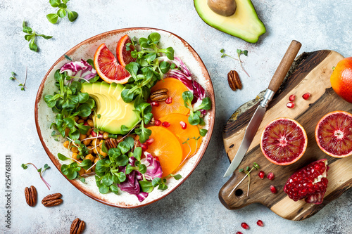 Vegan, detox Buddha bowl with turmeric roasted  chickpeas, greens, avocado, persimmon, blood orange, nuts and pomegranate. Top view, flat lay photo