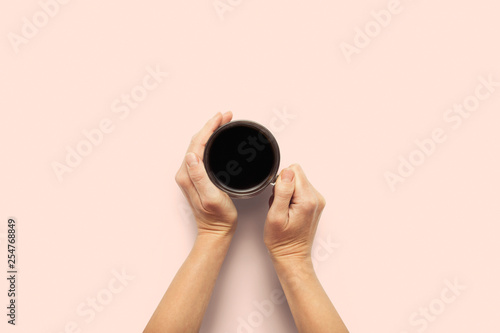 Two hands holding a cup with hot coffee on a pink background. Breakfast concept with coffee or tea. Good morning, night, insomnia. Flat lay, top view