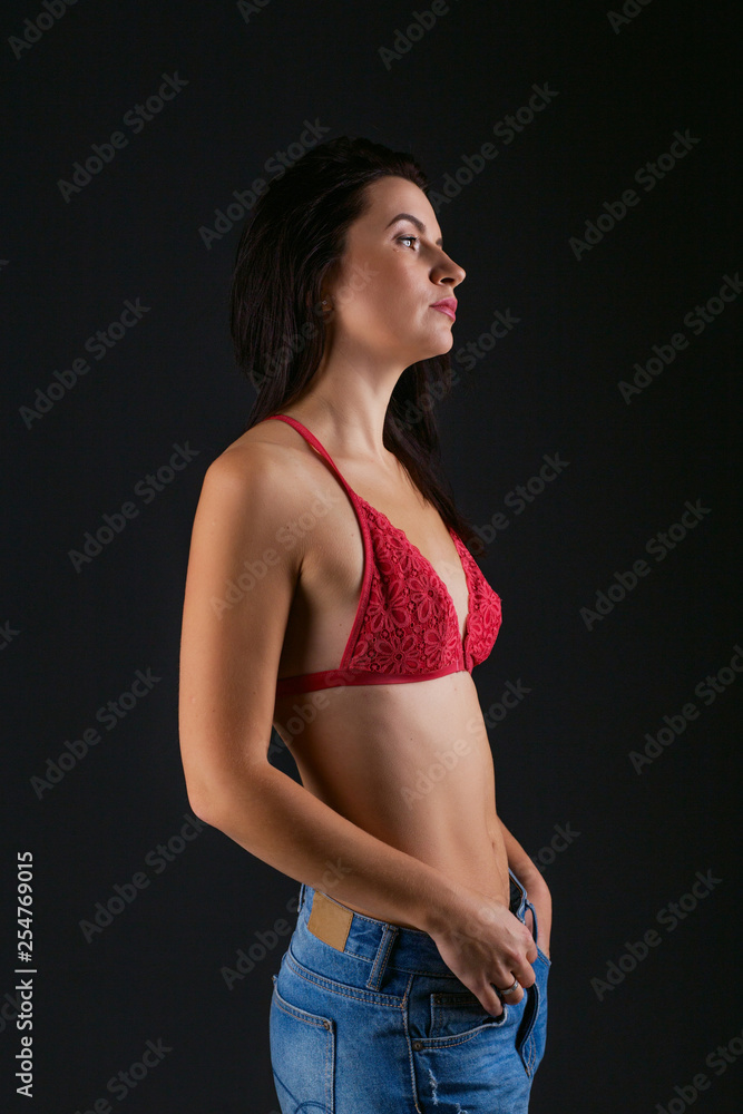 Beautiful sporty lady in red bra and blue jeans against dark