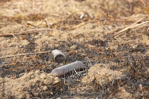 An empty glass charred bottle is lying on grass that has been baked out. Ecological catastrophy. Spring tan green cover. Danger of fire. The destruction of life and pollution. Problems of civilization