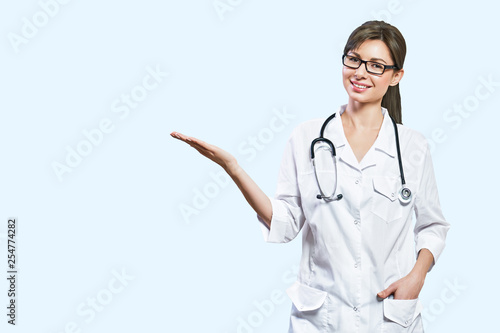 Billede på lærred Friendly smiling young female doctor. hand pointing at copy space