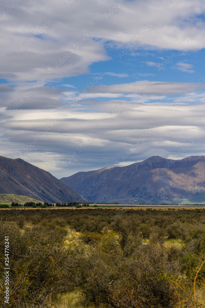 Vast valley with mountain range on the horizon, shadow play on mountain hills and dramatic sky during warm and sunny day Vast valley with mountain range on the horizon, shadow play on mountain hills and dramatic sky during warm and sunny day