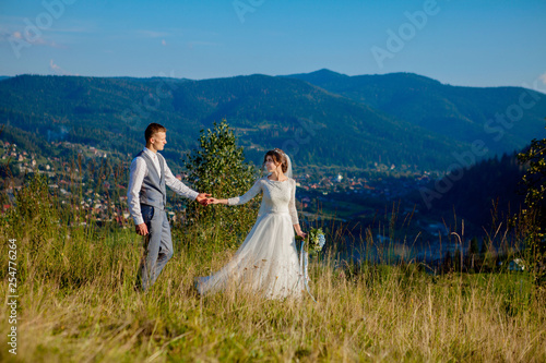 Newlyweds smile and hug each other among the meadow on top of the mountain. Wedding walk in the woods in the mountains  the gentle emotions of the couple  photo for Valentine s Day