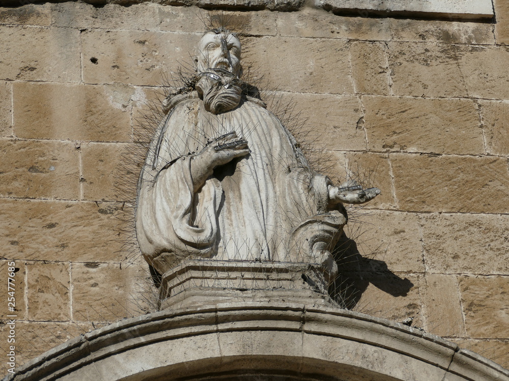 Statua antica ricoperta di filo spinato in ferro per tenere lontano gli uccelli. Chiesa Santa Lucia. Bari, sud Italia