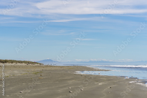 Beautiful empty beach during sunny day with mountains on the horizon, costal line with blue sky