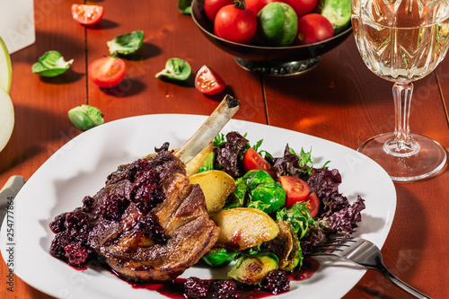 Roasted ribs in blackbarry sauce with vegetables, brussels sprout, cherry tomatoes and apple on wooden background photo