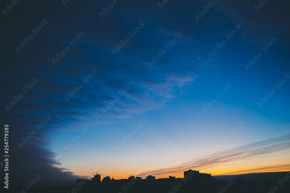 Cityscape with wonderful varicolored vivid dawn. Amazing dramatic blue cloud sky above dark silhouettes of city building roofs. Atmospheric background of orange sunrise in overcast weather. Copy space Cityscape with wonderful varicolored vivid dawn. Amazing dramatic blue cloud sky above dark silhouettes of city building roofs. Atmospheric background of orange sunrise in overcast weather. Copy space
