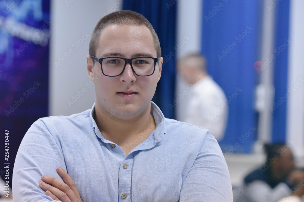 Group of students study in modern school classroom. Male student wearing glasses looking into camera. Group of students study in modern school classroom. Male student wearing glasses looking into camera.