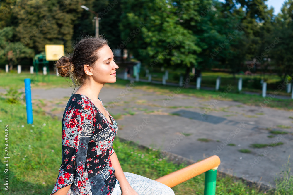 Happy girl woman side closeup smiling looking to side profile sitting on horizontal bars parallel bars exercise in outdoor park in Rivne, Ukraine track field basketball court Happy girl woman side closeup smiling looking to side profile sitting on horizontal bars parallel bars exercise in outdoor park in Rivne, Ukraine track field basketball court