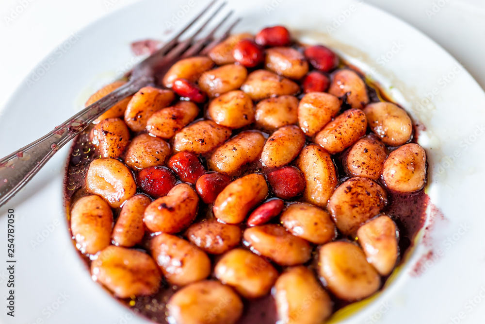 Closeup of fresh red wine sauce potato gluten free wheat gnocchi on white plate with lupine beans in Italian Italy restaurant with fork and olive oil Closeup of fresh red wine sauce potato gluten free wheat gnocchi on white plate with lupine beans in Italian Italy restaurant with fork and olive oil