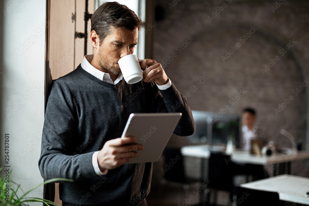 businessman drinking coffee while using digital tablet by the window in the office. businessman drinking coffee while using digital tablet by the window in the office.
