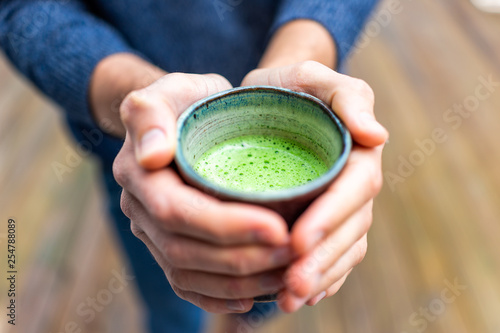 Macro closeup of man person hands holding tea cup outside on backyard deck wooden bokeh background in garden drinking matcha green drink in spring or autumn season photo