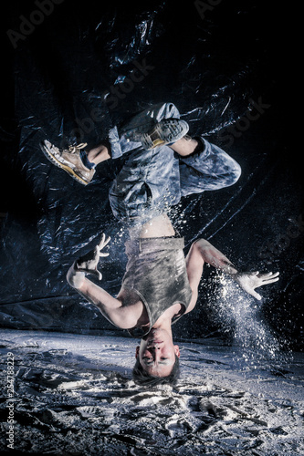 cool dirty сhinese guy dancer in style of bboying doing complex tricks on floor in Studio filled with flour on black background. concept of space dance on surface of planet moon photo