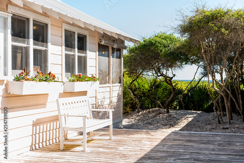 Fototapeta Naklejka Na Ścianę i Meble -  Wooden bench and cottage home house architecture in Florida beach by sand dunes during sunny day peaceful tranquil vacation