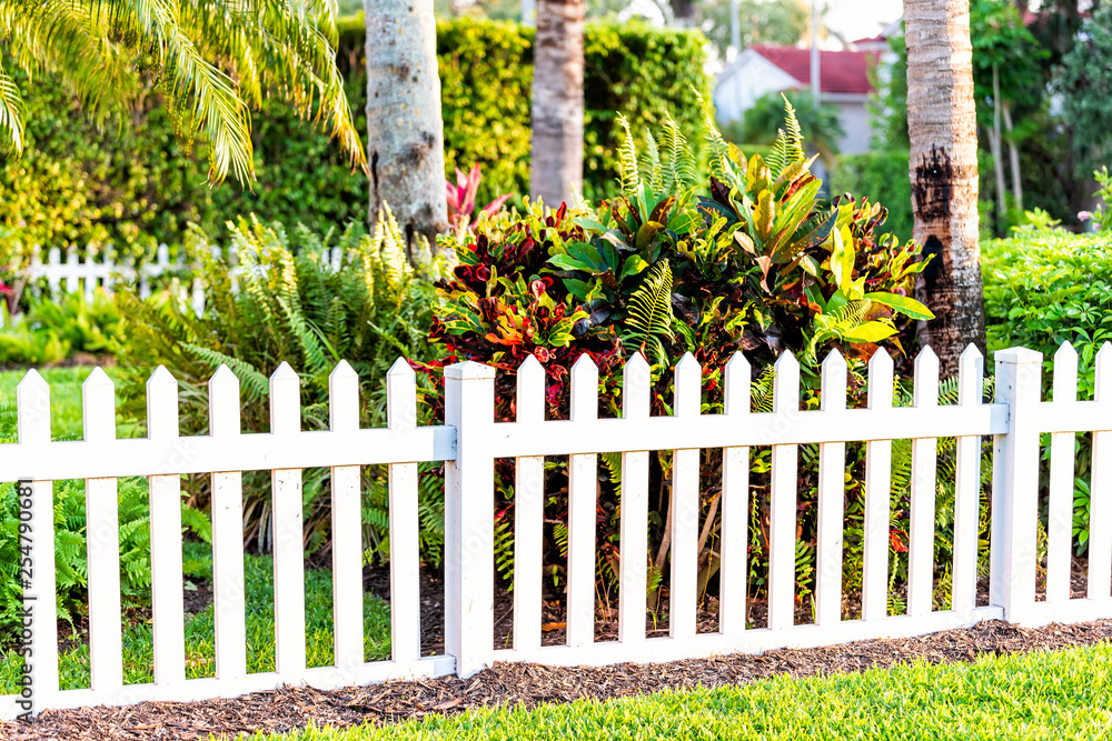 White beach wooden wood architecture picket fence of house in front porch yard garden with green landscaping trees vacation cottage home closeup White beach wooden wood architecture picket fence of house in front porch yard garden with green landscaping trees vacation cottage home closeup