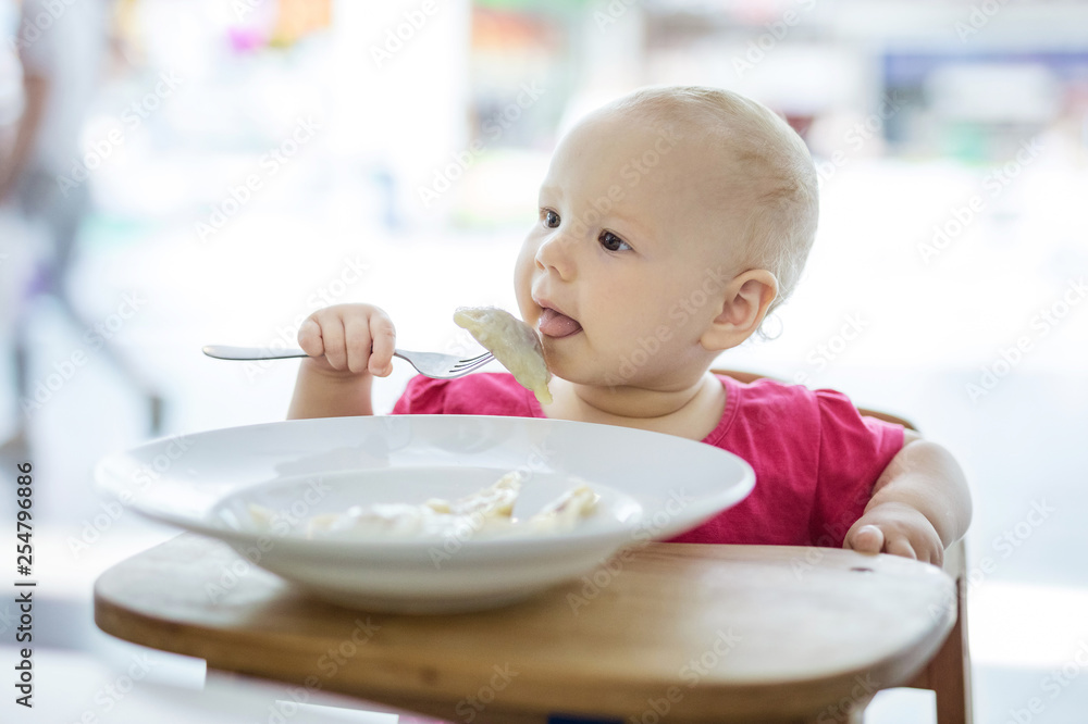 Little girl sitting in high chair and eating dumplings Little girl sitting in high chair and eating dumplings