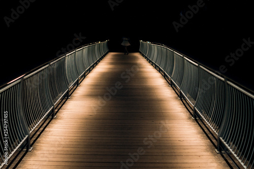 Blurry figure dances at end of long illuminated bridge