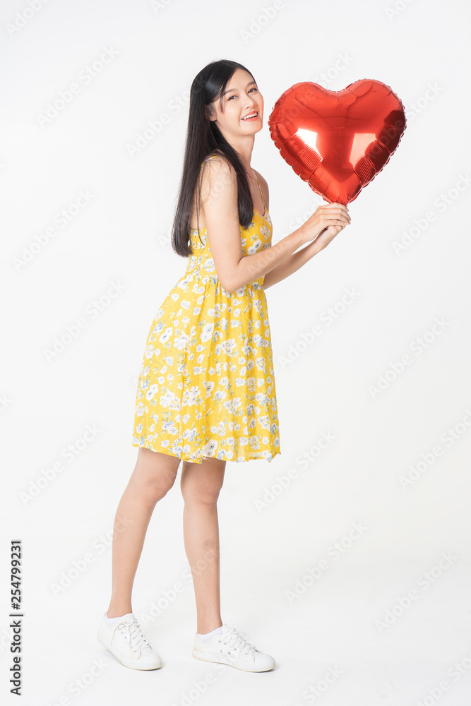 Asian young woman in yellow dress hold red balloon heart. Young woman holding it with being excited and surprised holiday present isolated white background.concept love surprise valentine day. Asian young woman in yellow dress hold red balloon heart. Young woman holding it with being excited and surprised holiday present isolated white background.concept love surprise valentine day.