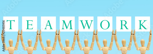 Group of wooden figure mannequin standing and holding text label in words Teamwork.