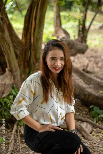 Women white skin lovely brown hair red lip wear white shirt wearing black pants women sit poses photography portrait under the tree In the garden.