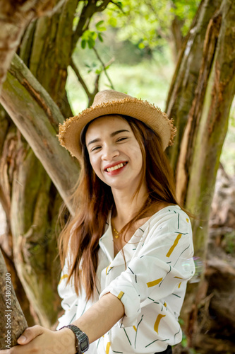 Women white skin lovely brown hair wearing a basketry hat brown red lip wear white shirt wearing black pants women sit poses photography portrait under the tree In the garden.
