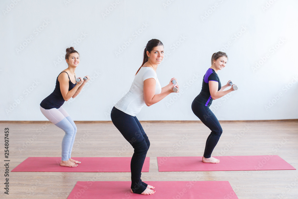 Group fitness in a bright and large room. Three young girls are engaged in group fitness against a white wall. Group fitness in a bright and large room. Three young girls are engaged in group fitness against a white wall.