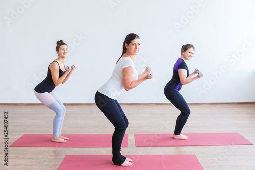 Group fitness in a bright and large room. Three young girls are engaged in group fitness against a white wall.