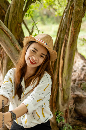 Women white skin lovely brown hair wearing a basketry hat brown red lip wear white shirt wearing black pants women sit poses photography portrait under the tree In the garden.