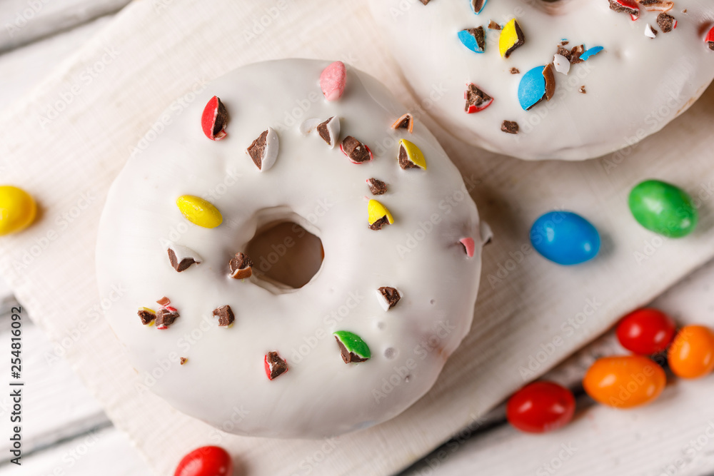 Cookery, baking and food concept - closeup. Donut in white glaze with color dragee on the decorative board top view. Cookery, baking and food concept - closeup. Donut in white glaze with color dragee on the decorative board top view.