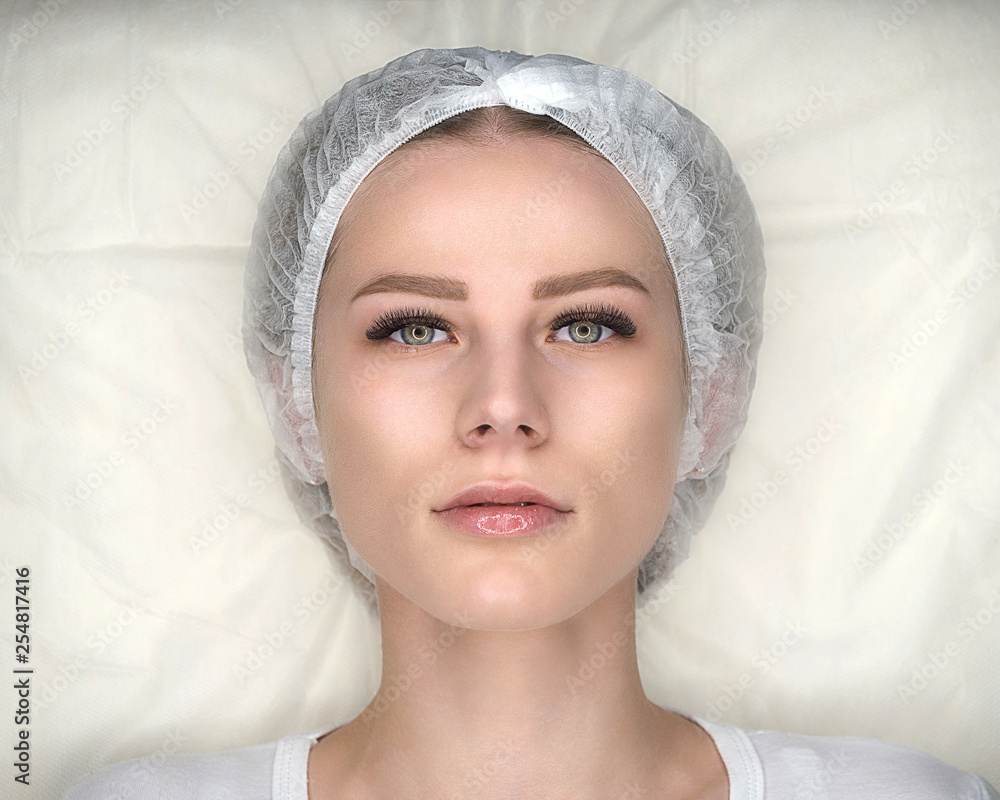 Female face with new false lashes and in disposable cap, eyelash extension procedure. Close up, top view Female face with new false lashes and in disposable cap, eyelash extension procedure. Close up, top view