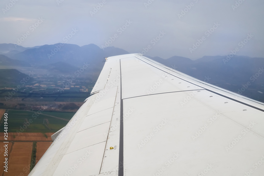 View of airplane wing over clouds and mountains during take off or landing in airport