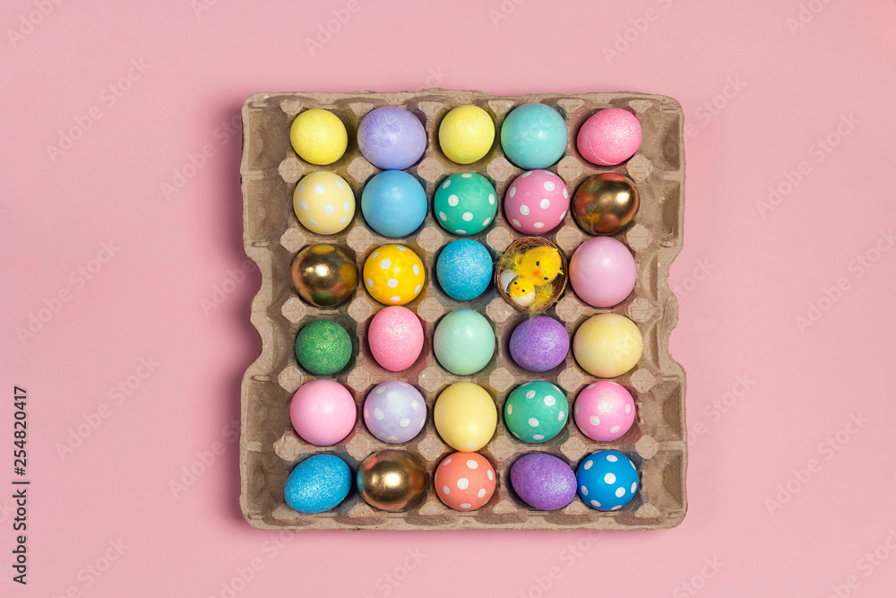 Many colored Easter eggs on tray on a pink background.