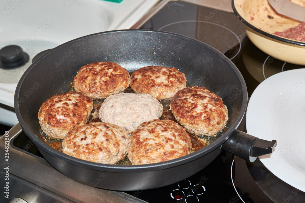 Beef and pork meat patties are roasted in a pan on a gray-colored electric stove in the kitchen at home. homemade delicious food. cooking at home. hearty dinner