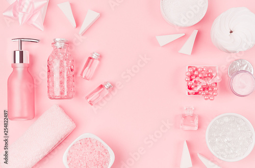 Cosmetic products and accessories in pink color - cream, bath salt, essential oil, soap, towel, sponge, pearls, bottles, bowl on pink background, copy space.